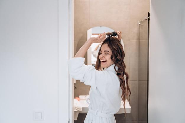 Happy woman styling her hair in bathroom mirror