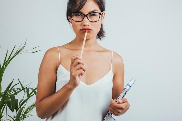 A woman with glasses holding a pencil and a notebook, looking thoughtful.