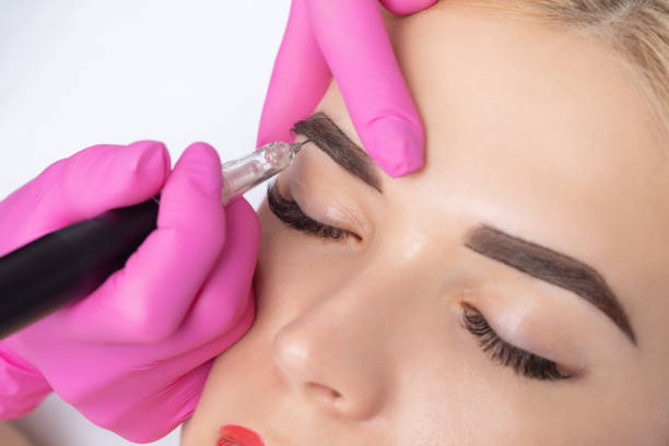 Microblading treatment on woman's eyebrows with beautician using tool