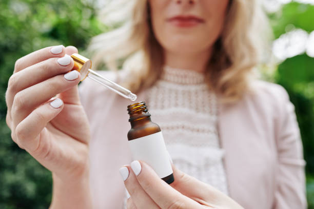 Woman Using Essential Oil Dropper - Close-up of a woman in a pink outfit using a glass dropper to dispense essential oil from a small brown bottle